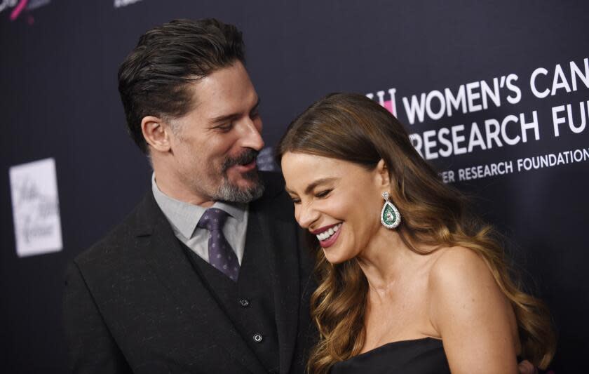 Sofia Vergara in a black dress and Joe Manganiello in a black suit are laughing together while posing for photos