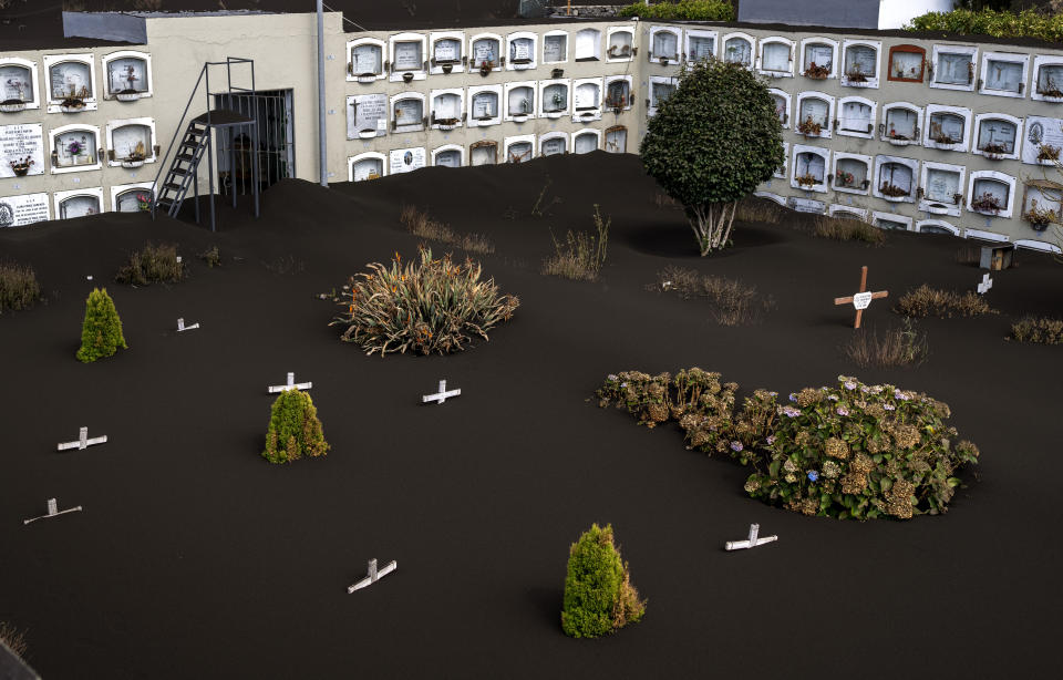 Ash cover the graves at the La Palma cemetery as volcano continues to erupt on this Canary island, Spain, Friday, Oct. 29, 2021. An erupting volcano in the Spanish island of La Palma continued to emit vast amounts of magma, gases and ash, after days of intense seismic activity and more than five weeks since it erupted. (AP Photo/Emilio Morenatti)