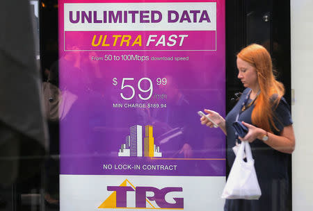 A woman looks at her phone as she walks past an advertisement for Australia's TPG Telecom Ltd in central Sydney, Australia, April 12, 2017. REUTERS/Steven Saphore