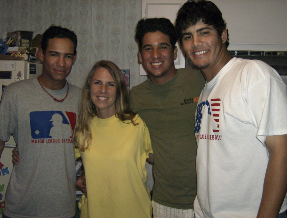 In this photo provided by TeriAnn Reynolds, minor league baseball player Eduardo Sánchez, left, poses with host TeriAnn Reynolds, and minor league baseball players David Peralta, second from right, and Reynier González in the Reynolds residence in Johnson City, Tenn., in August 2007. TeriAnn Reynolds and her family were part of a little-known but vital piece of baseball's minor leagues for decades: host families. Players at the lower levels of the minor leagues in places like Johnson City or Lake Elsinore, California, often stayed at the homes of local families instead of apartments or hotels — a way to save money for low-wage players as they transitioned into their lives as pro athletes. (Photo courtesy TeriAnn Reynolds via AP)