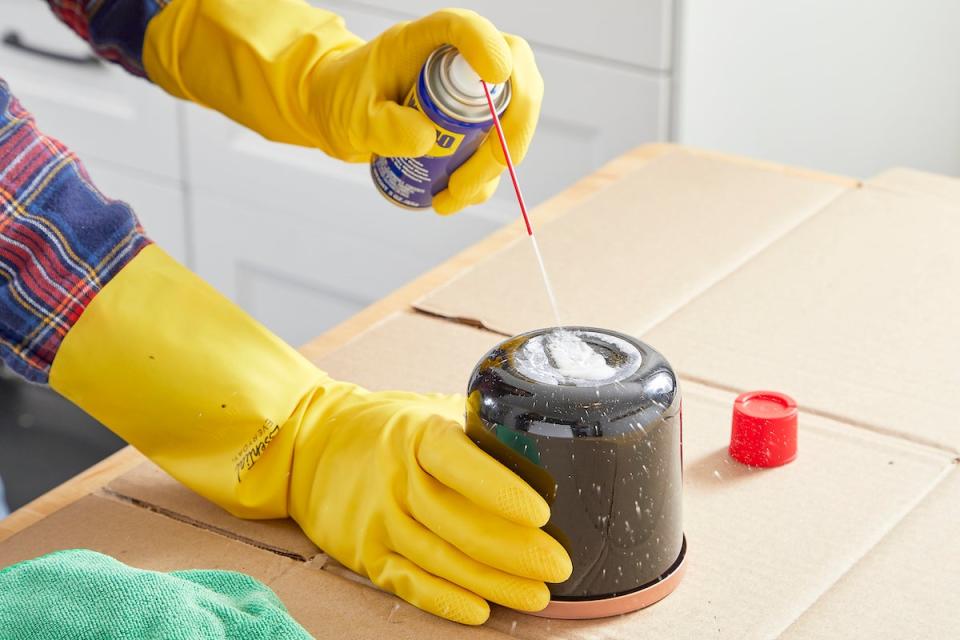 Woman sprays WD-40 to remove sticker on a jar.