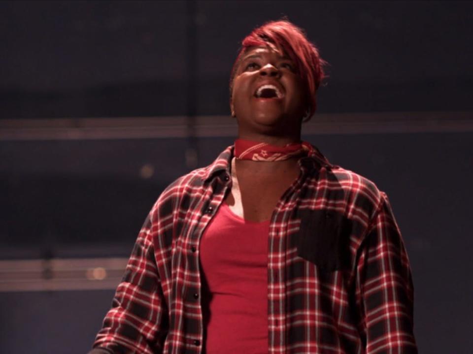 ester dean, with bright red short hair, singing powerfully on a stage, looking slightly up with her eyes closed