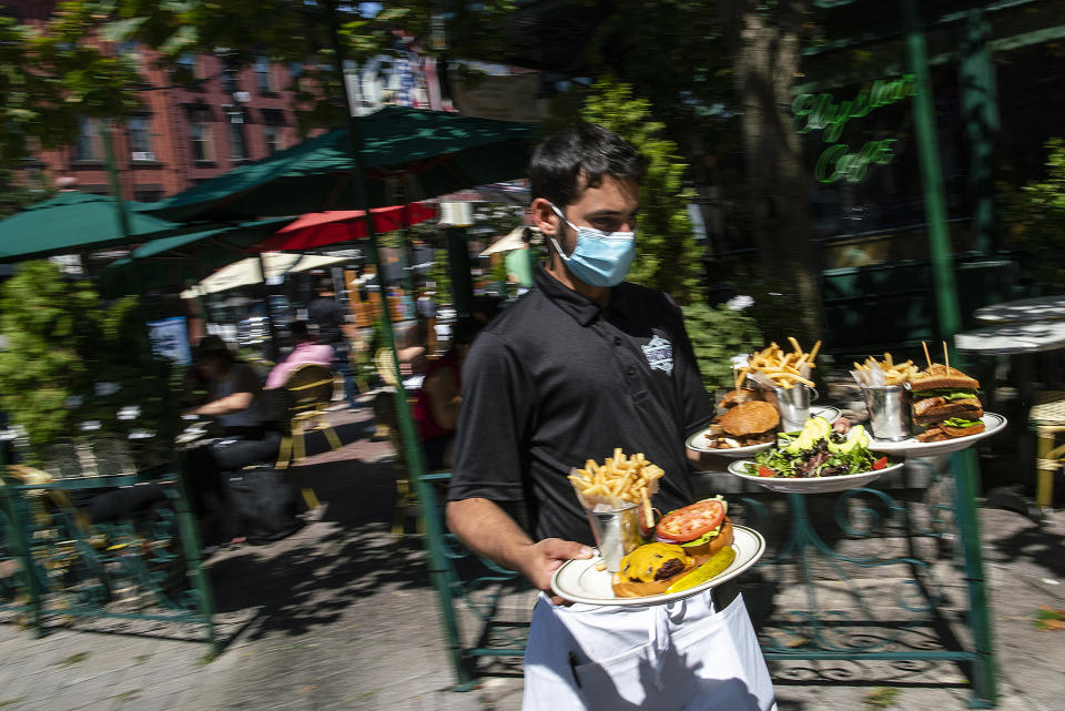 Un camarero con una mascarilla para protegerse del coronavirus entrega comida en la sección al aire libre de un restaurante, el viernes 4 de septiembre del 2020, en Hoboken, Nueva Jersey. (AP Foto/Eduardo Muñoz Alvarez)