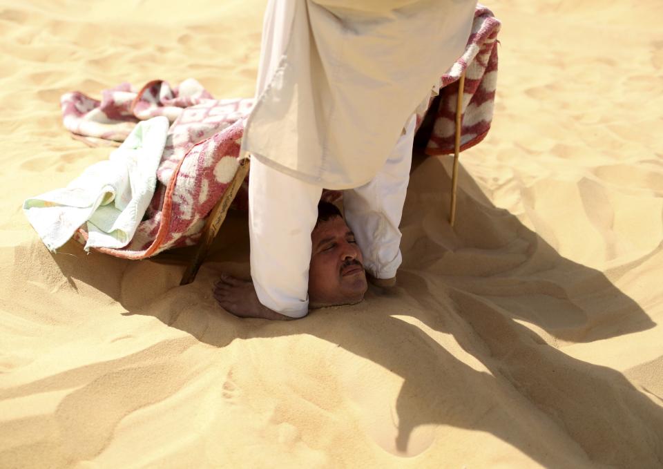 A worker gives a massage to a patient buried in sand by pressing on his shoulders with his feet in Siwa, Egypt, August 12, 2015. (REUTERS/Asmaa Waguih)