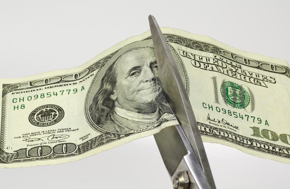 Scissors cutting through a $100 bill.