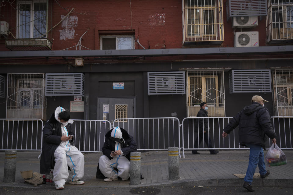 FILE - Workers in protective gear browsing their phones keep watch outside a locked down neighborhood as part of COVID-19 controls in Beijing, Nov. 23, 2022. (AP Photo/Andy Wong, File)