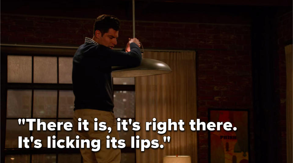Schmidt is standing on a table holding the light fixture and says, There it is, it's right there, it's licking its lips