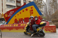 FILE - In this March 19, 2021, file photo, residents wearing masks ride pass government propaganda with slogans some of which read "Forever follow the Party" and "China's Ethnicities One Family" in the city of Aksu in western China's Xinjiang region. A human rights group appealed to the United Nations on Monday, April 19, 2021 to investigate allegations China's government is committing crimes against humanity in the Xinjiang region. (AP Photo/Ng Han Guan, File)