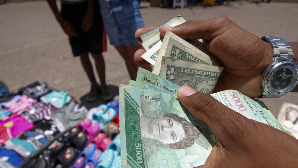 Hombre sostienen dólares y bolívares