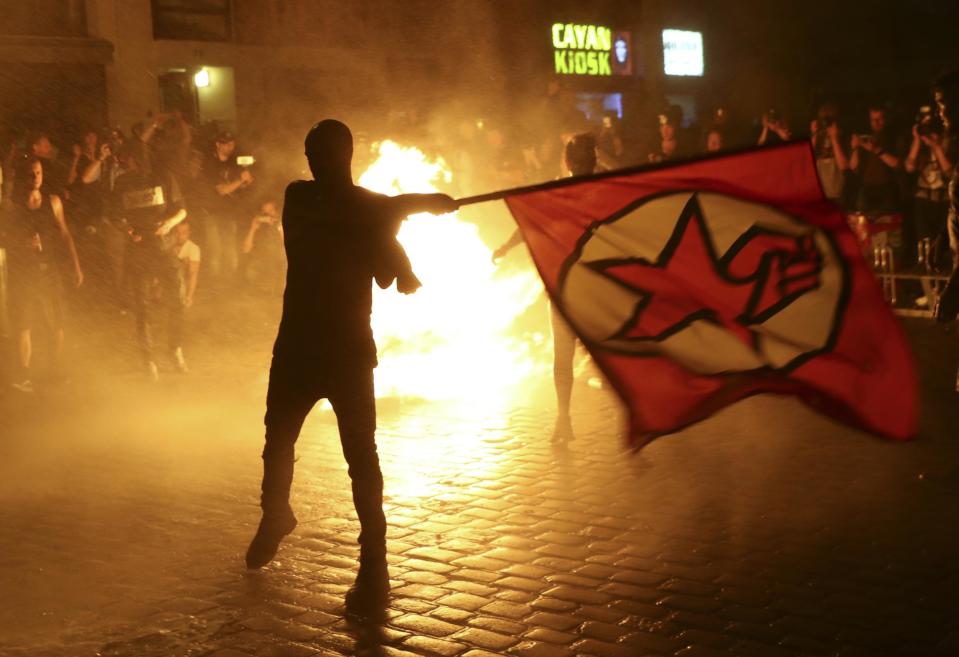 An anti-G20 protester waves a flag in front of burning garbage following clashes with German riot police in Hamburg, Germany, July 6, 2017: REUTERS