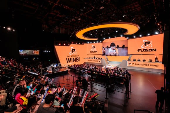 An audience watching a brightly lit stage during an Overwatch League match.