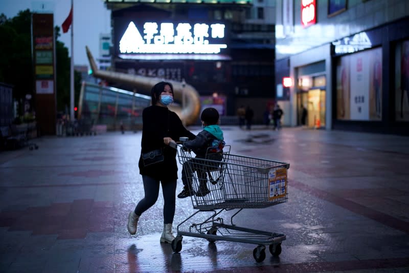 Woman wearing a face mask pushes a shopping trolley with a child sitting on it outside a shopping mall in Xianning