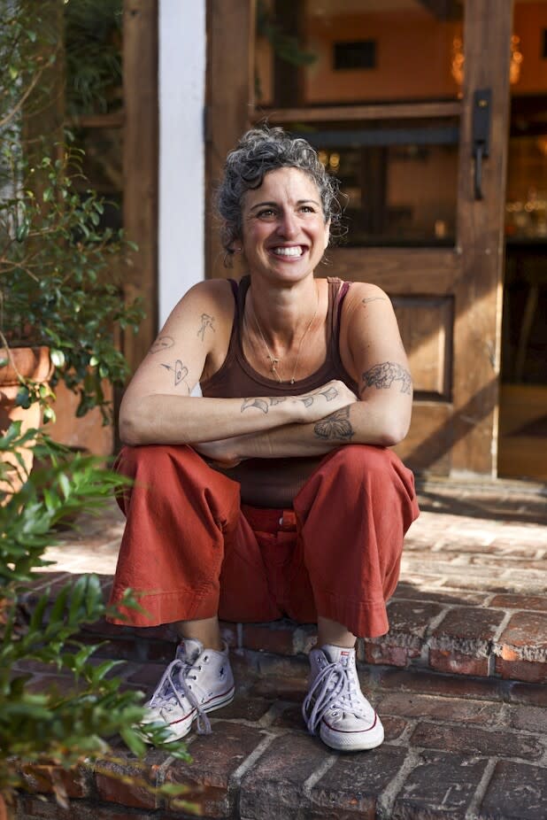 A smiling woman sits with her arms crossed