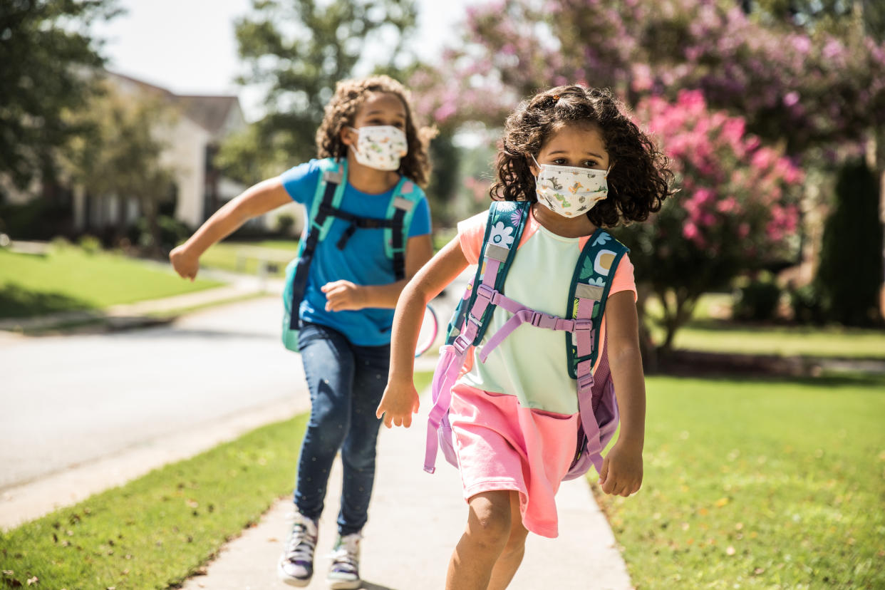 Young girls wearing protective masks running on sidewalk.