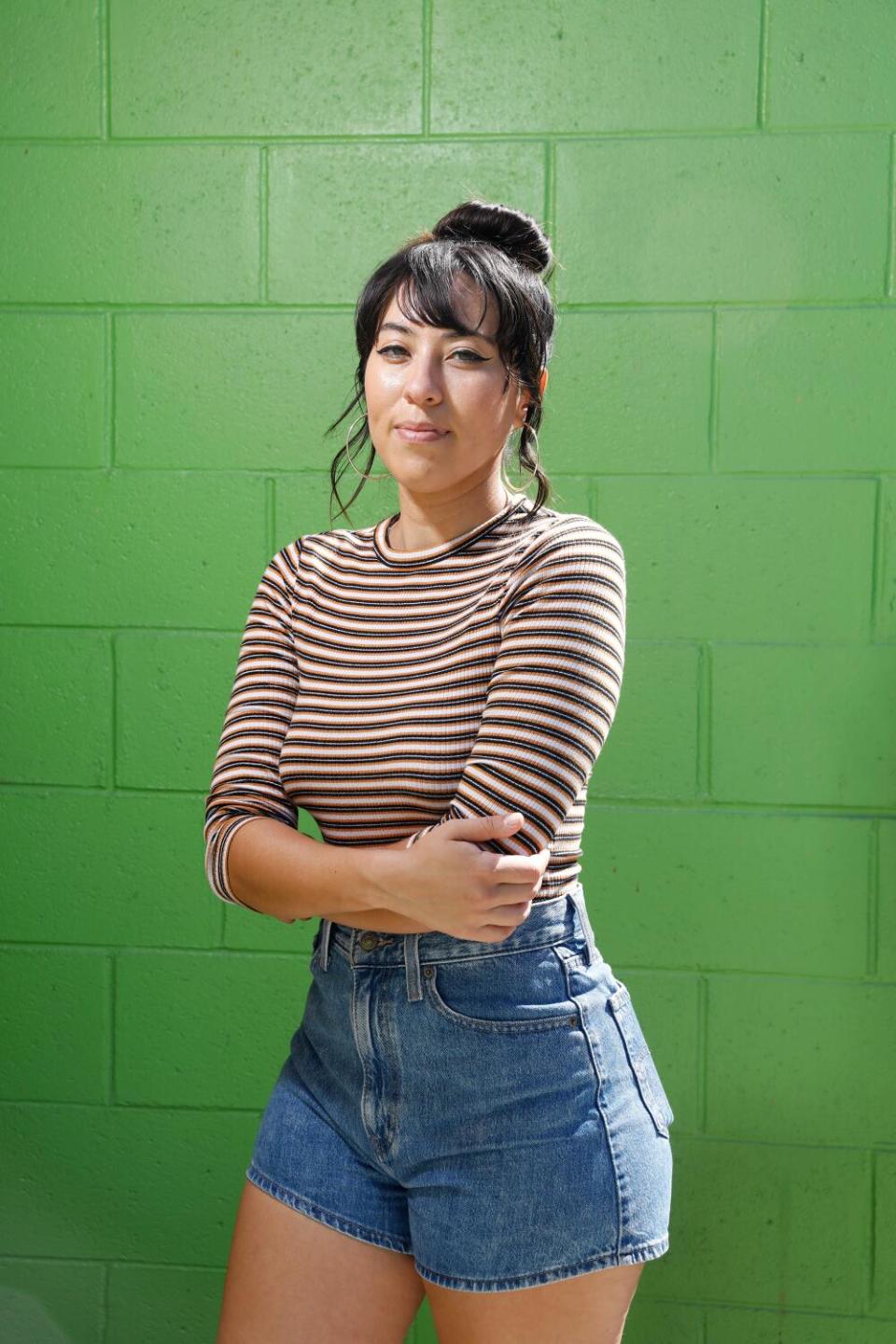 SueEllen Mancini stands against a green wall, arms crossed.