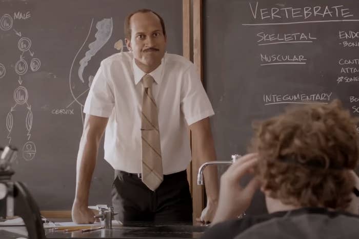 Keegan-Michael Key stands in a classroom leaning on a desk, teaching a lesson on vertebrate anatomy with detailed notes on a chalkboard in a scene from a comedy skit