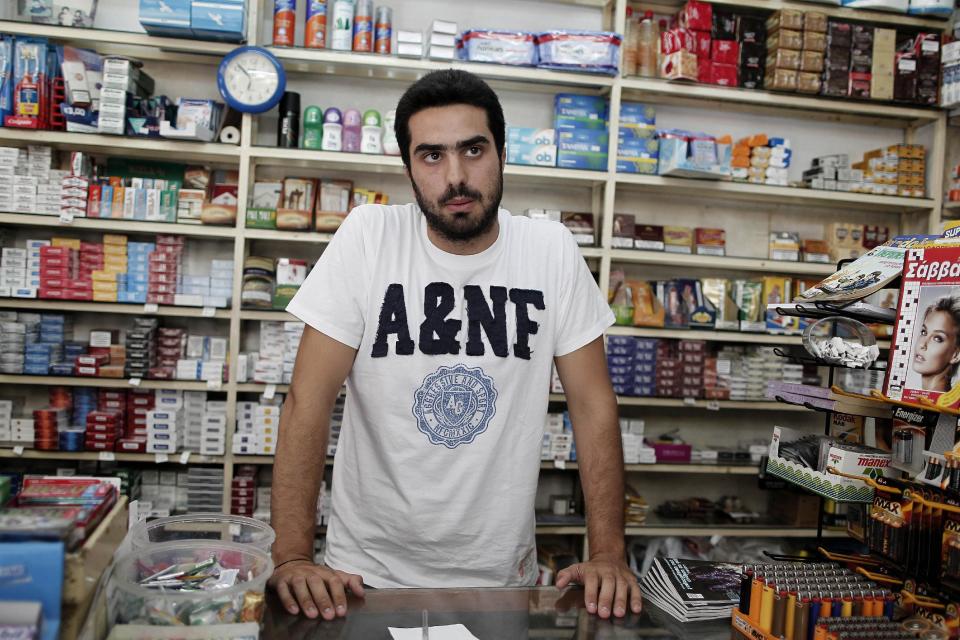 WITH STORY GREECE VOICES BY NIKOS PAPHITIS : Dimitris Dedoussis, 20, stands at the counter of his corner shop near Syntagma Square in central Athens, on Thursday, Aug. 23, 2012. As Greek Prime Minister Antonis Samaras sets off around Europe to plead for more time to achieve the country’s tough reform targets, austerity-weary Greeks are bracing for new pain but mostly expect to stay in the 17-nation eurozone, come what may. Dedoussis said planned new cutbacks would have severe consequences on Greece’s battered middle class, adding that he expects protests sooner or later because people won’t be able to cope. He said he does not expect the debt-crippled country’s partners will be able to kick Greece out of the currency union, and will instead “seek ways of taking the last euro left in our pockets.”(AP Photo/Petros Giannakouris)
