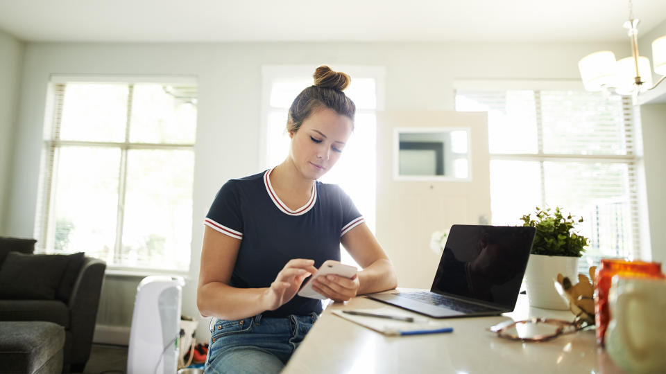 Shot of a young woman using a mobile phone while working at home.