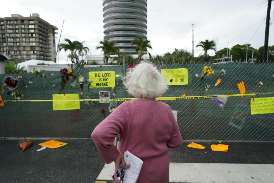 A person looks at a fence with flowers placed in it.