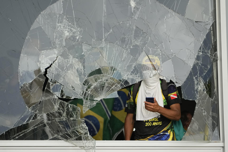 FILE - Supporters of Brazil's former President Jair Bolsonaro, look out from a shattered window after they stormed the Planalto presidential palace in Brasilia, Brazil, Jan. 8, 2023. A year later, around 400 people remain jailed facing charges for the riots and Bolsonaro has been under investigation by the Supreme Court about his role in the mayhem. (AP Photo/Eraldo Peres, File)