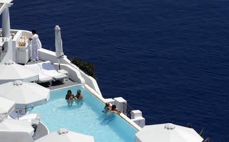 Tourists relax in a private swimming pool in the village of Oia on the Greek island of Santorini, Greece, July 1, 2015. REUTERS/Cathal McNaughton/Files