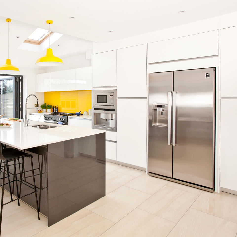 White kitchen with double silver American fridge freezer, island and yellow pendant lights