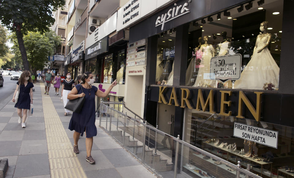 Women, wearing face masks to protect against the spread of coronavirus, walk past a bridal atelier that displays a masked mannequin, in Ankara, Turkey, Monday, Aug, 10, 2020.(AP Photo/Burhan Ozbilici)