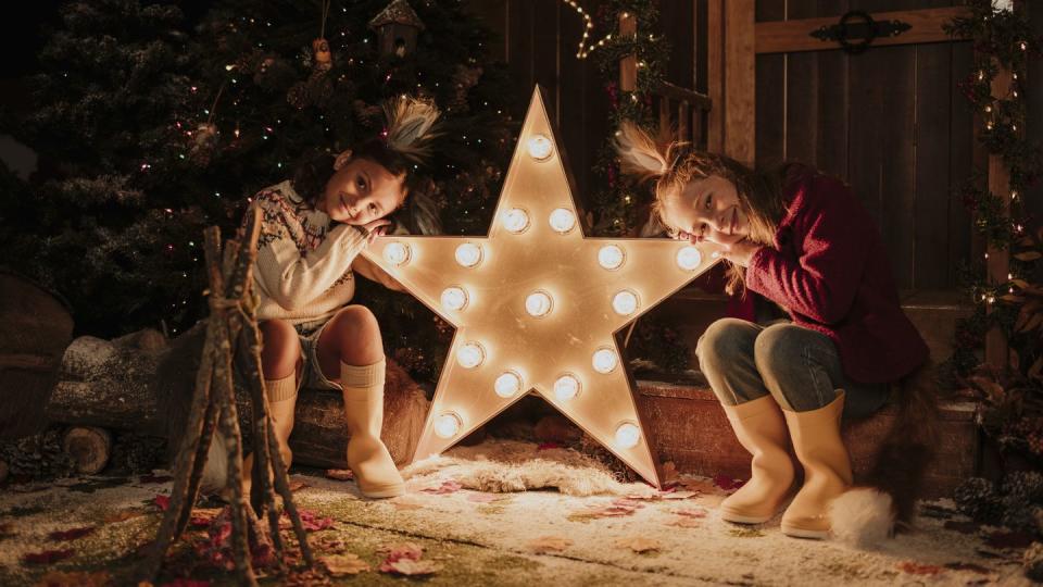 girls leaning head on illuminated start shape light at christmas