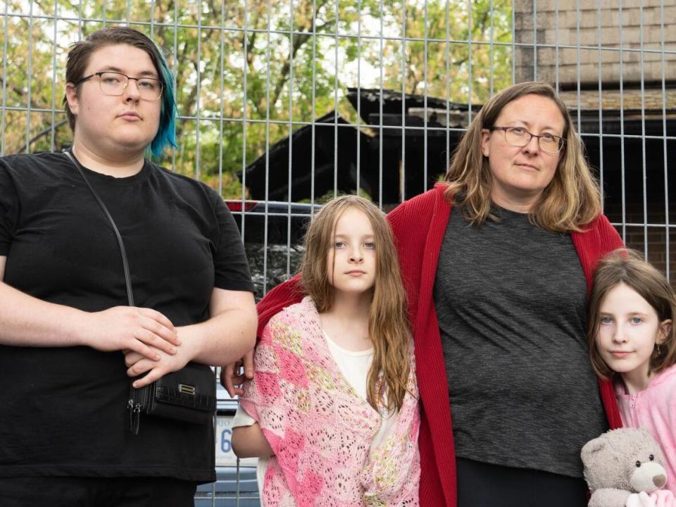 Some members of the Riggins family are pictured next to the home destroyed in a fire on May 24, three days after the May 21 storm. Liz Riggins, second from right, says she's grateful everyone's safe. (Jean Delisle/CBC - image credit)