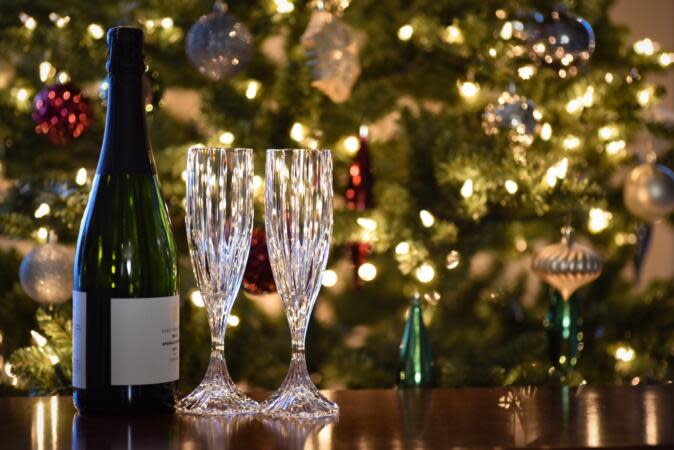 Check out this Christmas movie trivia to bring out at Christmas dinner. Pictured: a bottle of wine and two glasses on a table in front of a Christmas Tree. | 