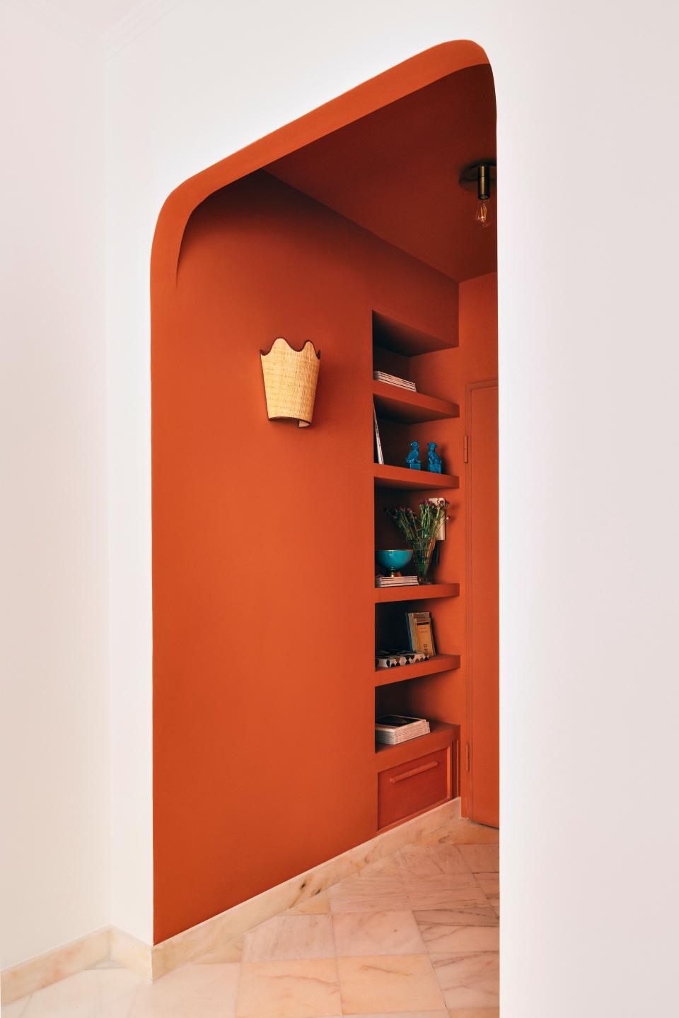 Mirta softened the entrance with arches and enveloped it in a warm coral. In a bid to optimize every square inch, she carved out a bookshelf on one wall and a full-height storage cabinet with three flush doors on the other. The ceiling lights are from H&M’s Markslöjd range, while the wavy-edged wall sconces, woven from raffia and Bordeaux grosgrain, are of Mirta’s own design.