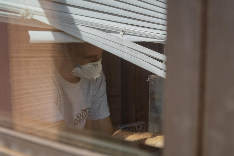 Daniel Skousen vacuums his home, damaged by August's wildfire, on Friday, Nov. 3, 2023, in Lahaina, Hawaii. Skousen stated he will not deep clean his home until the EPA removes all debris from the burnt house adjacent to his. (AP Photo/Mengshin Lin)