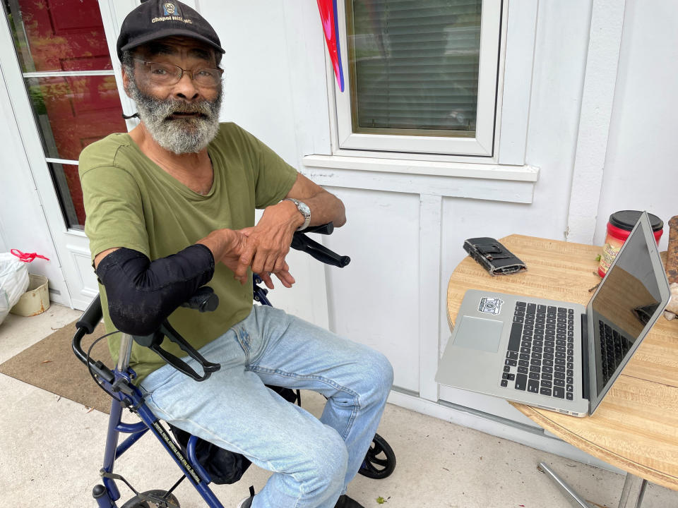 In this photo provided by The Rev. Lisa G. Fishbeck, Nathaniel “Pee Wee” Lee sits outside his home in Chapel Hill, N.C., on May 23, 2022. Fischbeck led the Episcopal Church of the Advocate when it added three one-bedroom units on its 15-acre campus. The first residents, including Lee, moved into them in June 2019. Before that Lee, 78, had spent years sleeping in alleys, cardboard shelters and cars after medical issues ended his bricklaying career. (The Rev. Lisa G. Fishbeck via AP)