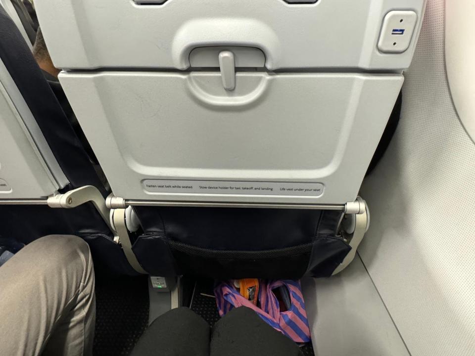 A view of a person's legs and the plane seat in front of them in economy class.