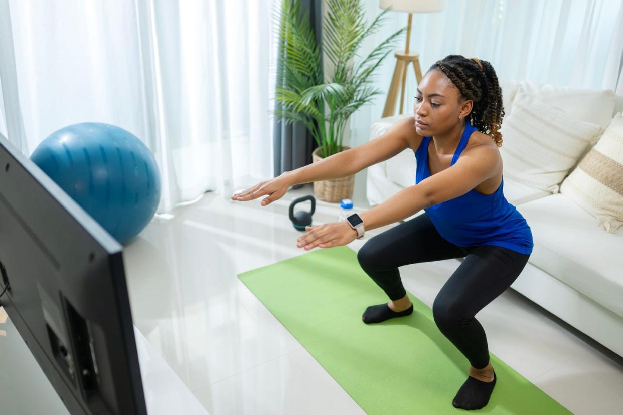 cardio squash is the best way to stay motivated in your training routine an african american woman doing squats in front of a smart tv during a home workout with an online class