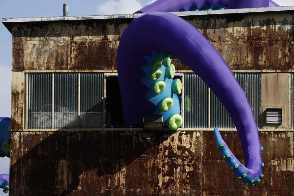 An inflatable sculpture entitled "Sea Monsters HERE" extends from a rusting warehouse called Building 61 at the Navy Yard in Philadelphia, Tuesday, Oct. 9, 2018. The installation was created by UK-based artists Filthy Luker and Pedro Estrellas. The former military base is free and open to the public. (AP Photo/Matt Rourke)