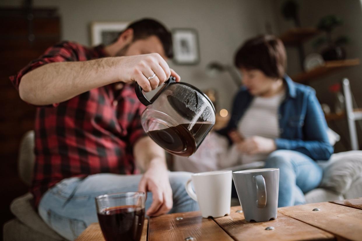 man pouring coffee at home with family in the background