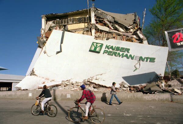 People bike past collapsed buildings