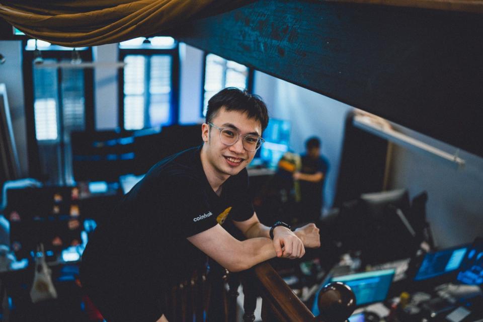 Image shows a man, SolanaFM co-founder and SMU undergrad Nicholas Chen, wearing glasses in a black T-shirt against a background of a startup office. 