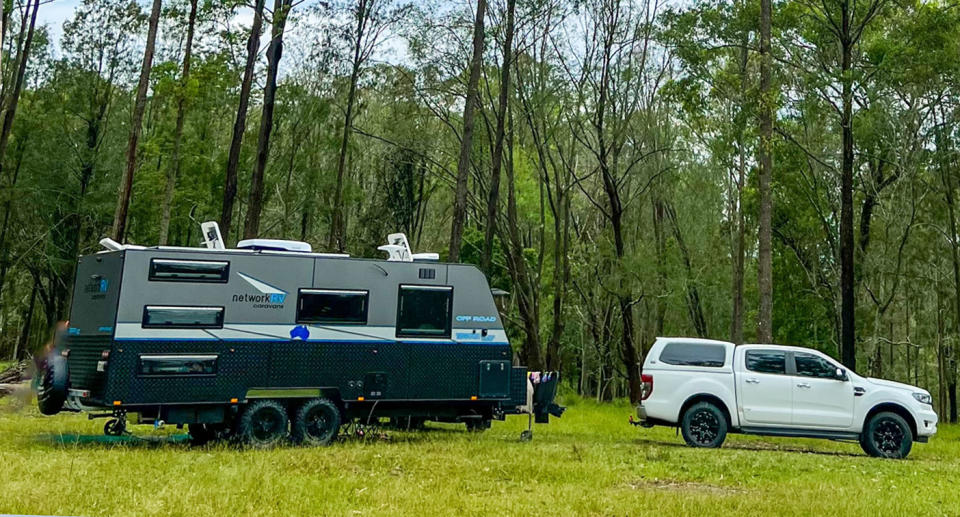 A white Ford Ranger ute and a caravan in a wooden area.