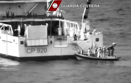 Italian coast guard officers stand on a dinghy beside an Italian coast guard vessel as a massive search and rescue operation is conducted at sea after a boat carrying migrants capsized overnight, in this still image taken from video April 19, 2015. REUTERS/Guardia Costiera/Handout via Reuters