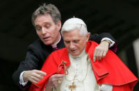 Pope Benedict XVI is helped by his personal secretary Georg Gaenswein as he puts on his red mantle after arriving at Saint Peter's Square at the Vatican, to lead his weekly audience, November 30, 2005. REUTERS/Max Rossi/File Photo