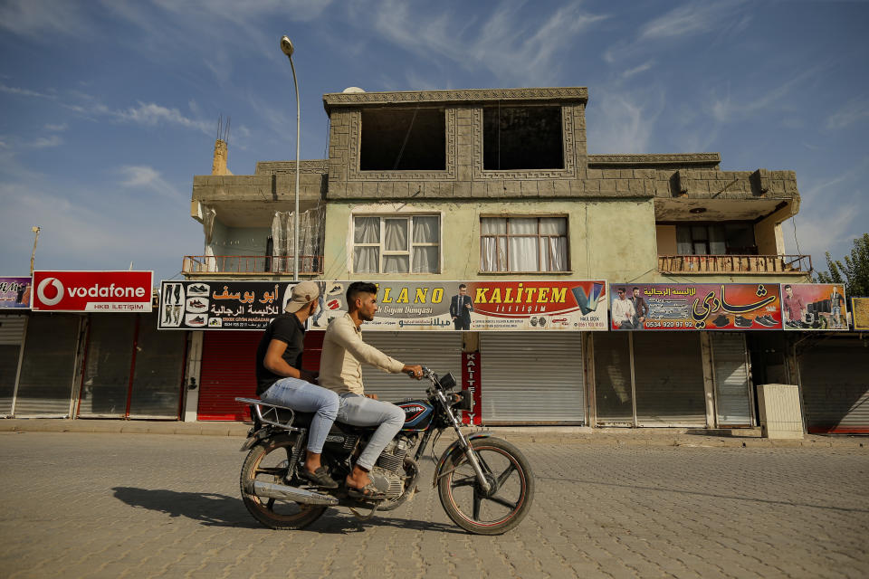 Youths drive past shops, closed by owners for fear of incoming shelling from Syria, in Akcakale, Sanliurfa province, southeastern Turkey, at the border with Syria, Friday, Oct. 11, 2019. The towns along Turkey's border with northeastern Syria have been on high alert after dozens of mortars fired from Kurdish-held Syria landed, killing at least nine civilians. (AP Photo/Emrah Gurel)