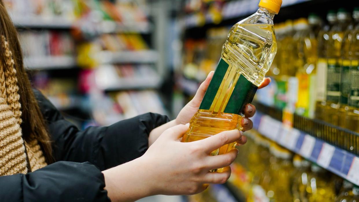 woman choosing sunflower oil in the supermarket close up of hand holding bottle of oil at store