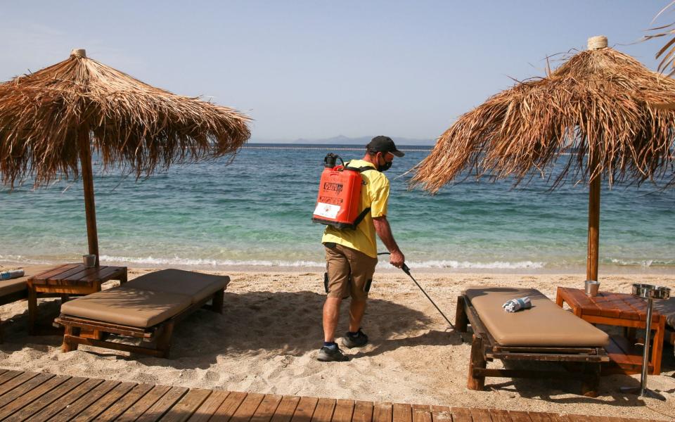 A man wearing a protective face mask disinfects a sunbed during the official reopening of beaches to the public, following the easing of measures against the spread of the coronavirus - REUTERS/Costas Baltas