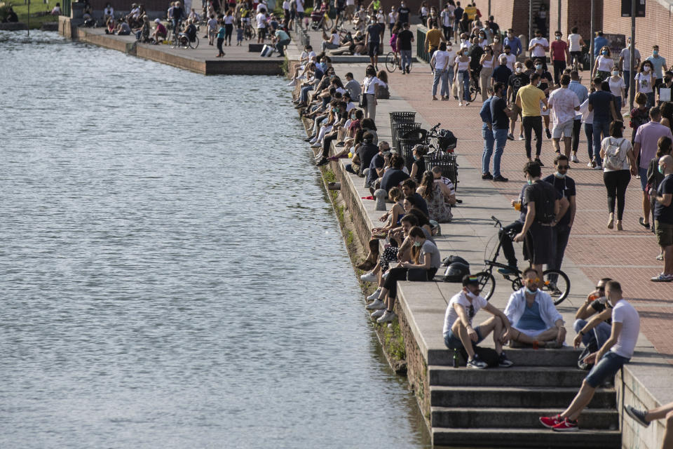 People relax at the Naviglio Grande canal, in Milan, Italy, Sunday, May 24, 2020. Europeans and Americans soaked up the sun where they could, taking advantage of the first holiday weekend since coronavirus restrictions were eased, while European governments grappled with how and when to safely let in foreign travelers to salvage the vital summer tourist season. Italy, which plans to open regional and international borders on June 3 in a bid to boost tourism, is only now allowing locals back to beaches in their own regions — with restrictions. (AP Photo/Luca Bruno)