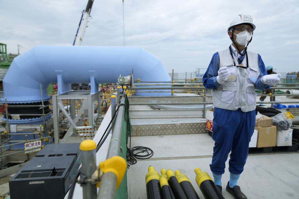 Tomohiko Mayuzumi, a spokesperson of Tokyo Electric Power Company Holdings, also known as TEPCO, speaks during a tour of the Fukushima Daiichi nuclear power plant for The Associated Press in Futaba town, northeastern Japan, Friday, July 14, 2023. He says treated radioactive water will be diluted with more than hundred times the seawater in this blue pipe, background, to levels much safer than international standards, before released into the sea. (AP Photo/Hiro Komae)