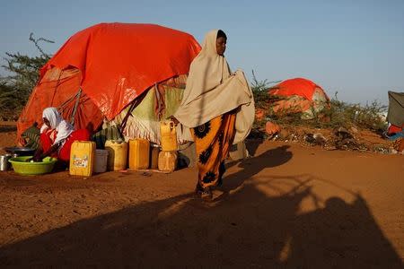 Abdir Hussein, 45, walks as she carries a jerrycan while her daughter Zeinab washes dishes at a camp for internally displaced people from drought hit areas in Dollow, Somalia April 4, 2017. REUTERS/Zohra Bensemra