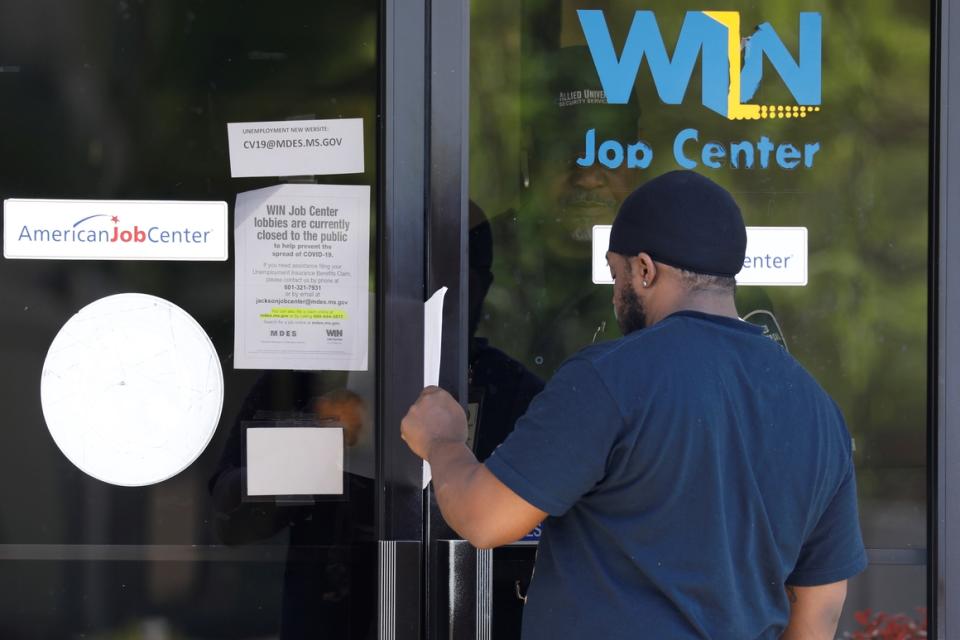 A Mississippi man is handed an unemployment benefit application form by a security guard behind glass doors  in north Jackson, Miss., on April 2, 2020.  