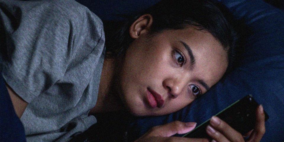 a young asian woman in bed in the dark looking at her phone